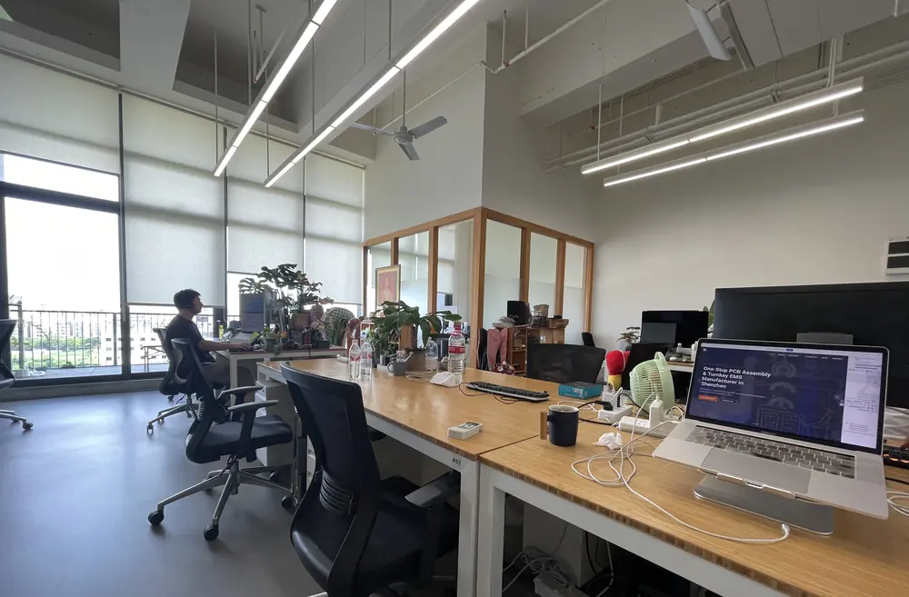 Open-plan office with desks, a laptop showing the BELI Technologies website and a colleague working by the window