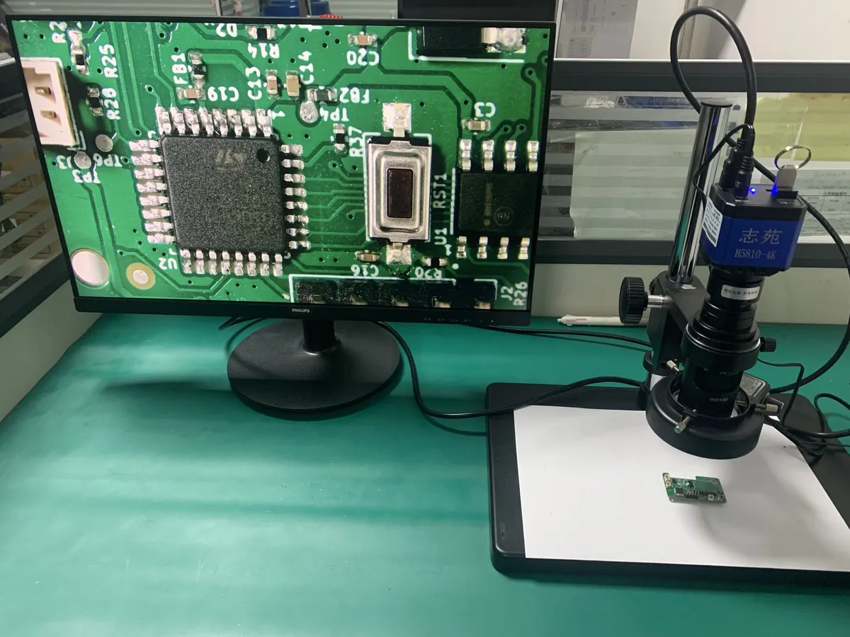 Assembled PCB under a 4K digital microscope, with the QFP solder joints magnified on the monitor at an inspection bench