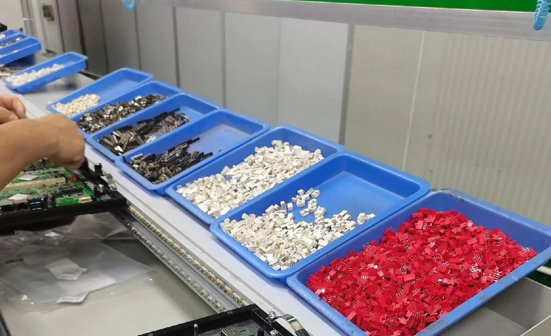 Operator sorting through-hole connectors and terminals in blue trays beside a board pallet on a conveyor line